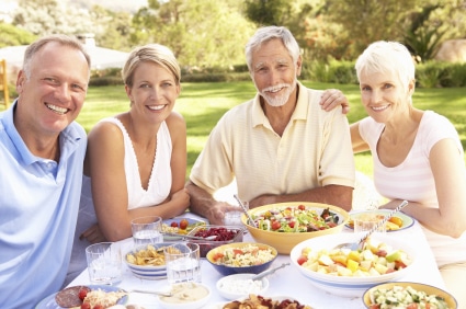 Adult Son And Daughter Enjoying Meal In Garden With Senior Parents