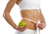 A fit woman holding a green apple measuring her waist to determine her metabolic health.