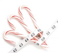Three Candy Canes wrapped in a measuring tape reminding us of holiday weight gain that usually happens this time of year.