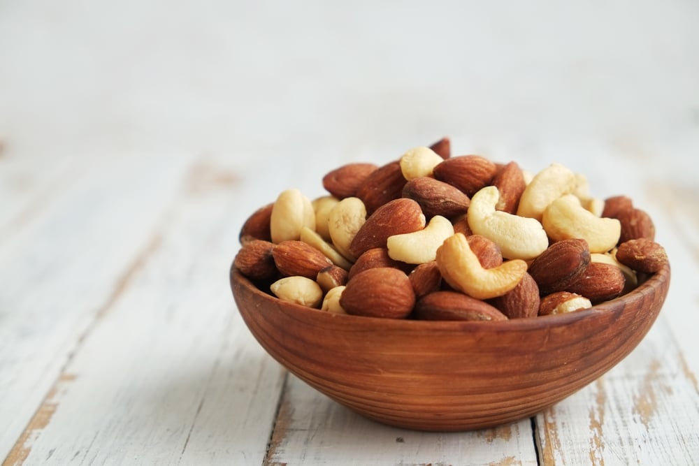 Mixed nuts, which are a brain healthy snack, in a bowl on a white wooden background.