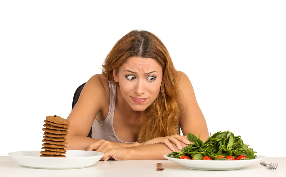 Young woman deciding whether to eat healthy food or sweet cookies loaded with unhealthy carbs