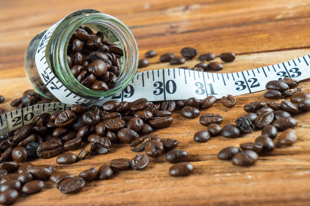 Coffee caffeine beans in glass bottle with tape measure on wooden table background