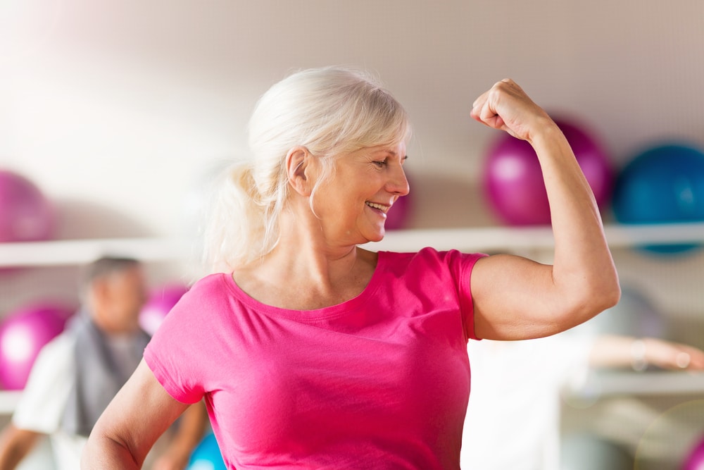 image of fit elderly woman proudly striking a bicep pose showing that strength training not only builds muscle, but also improves your metabolism.