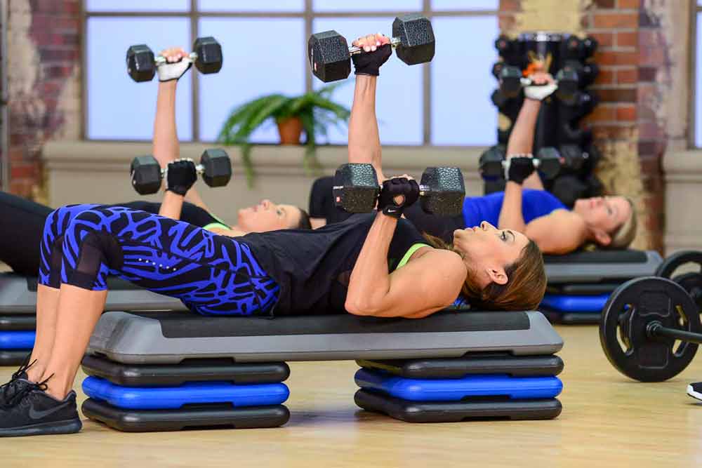 image of Cathe Friedrich doing a one arm dumbbell bench press in her Fit Split Push day workout DVD. Compound moves like this burn more calories