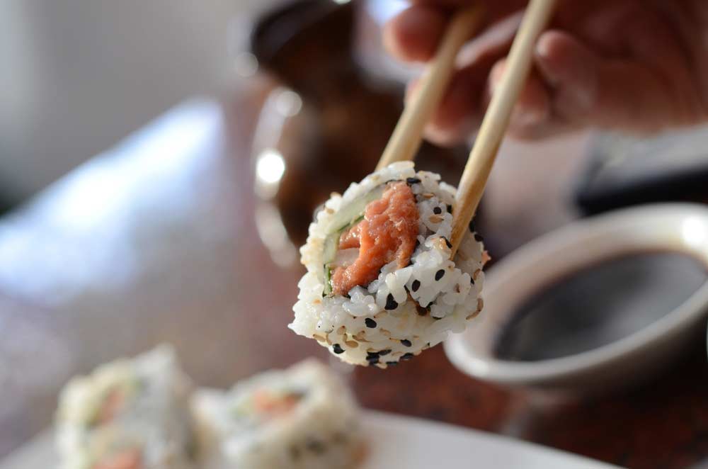 image of chopsticks holding Sushi. Chopsticks and focusing on your meal helps to prevent mindless overeating 