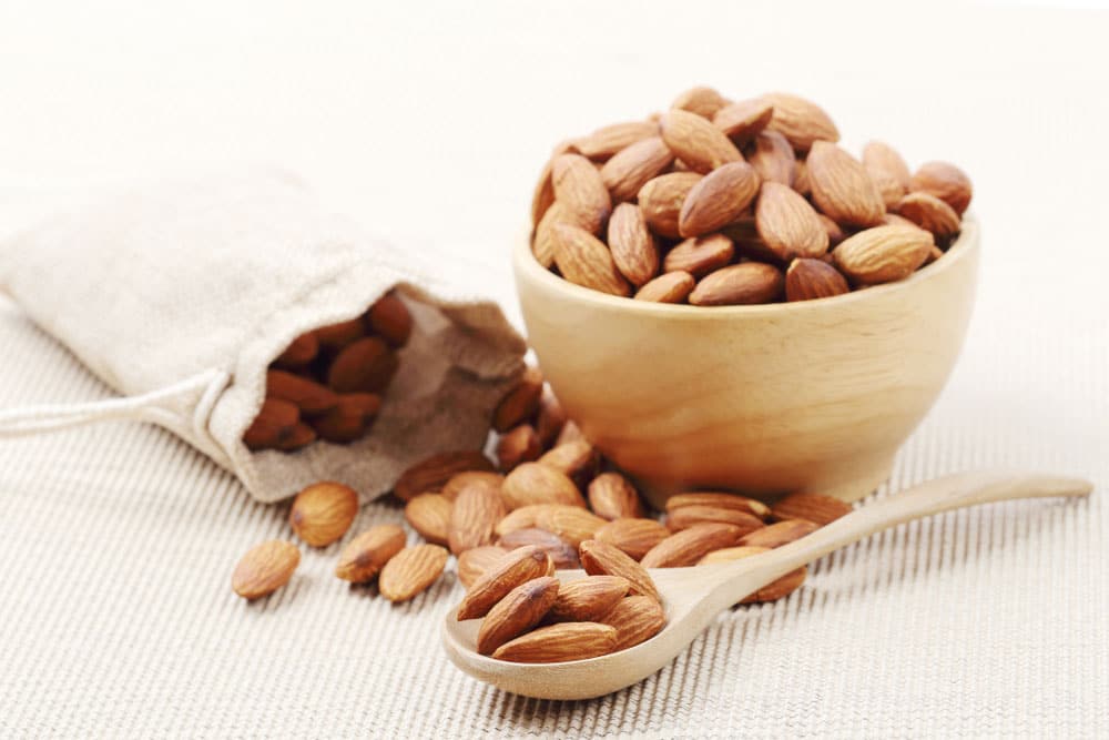 image of dry of almonds nuts in a wooden spoon over corrugated paper background. Eating nuts can result in a healthier body composition.