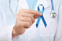 image of doctor holding blue ribbon, closeup. Cancer awareness concept