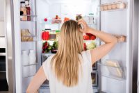 image of a young woman looking inside her refrigerator because she is hungry