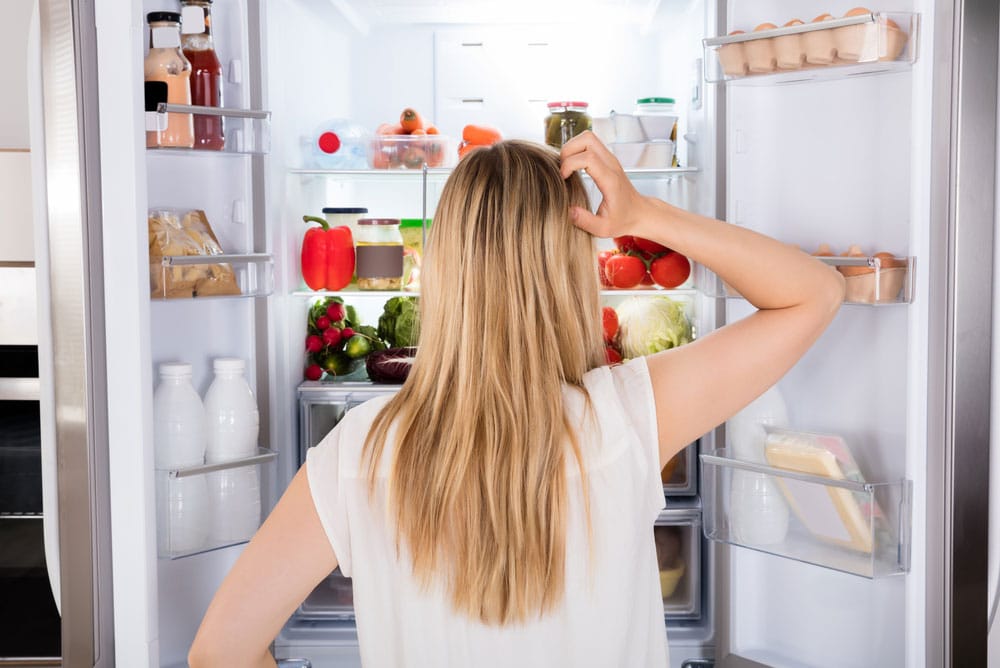 image of a young woman looking inside her refrigerator because she is hungry and not full after a meal