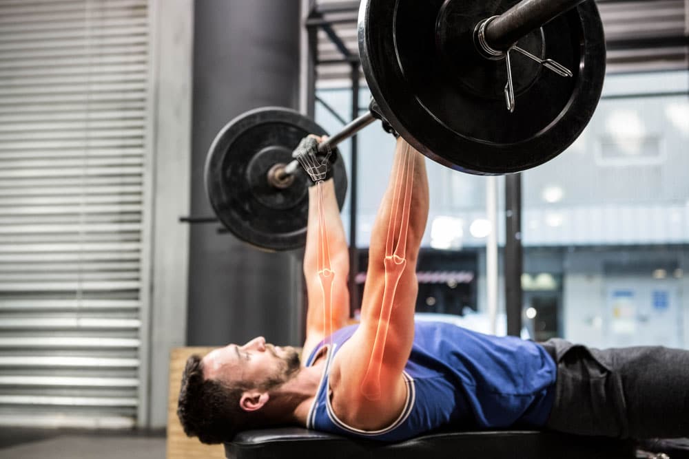 image of an athlete exercising doing a barbell bench press at a gym. Resistance training is great for bone health.