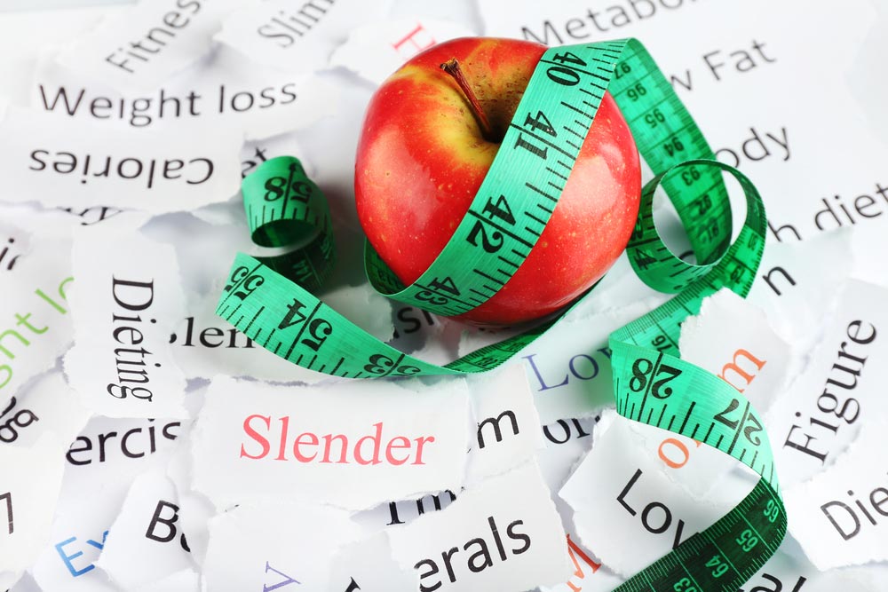 image of papers with different weight loss words, apple and measuring tape close up
