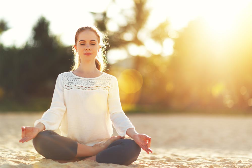 image of woman practices yoga and meditates in the lotus position on the beach