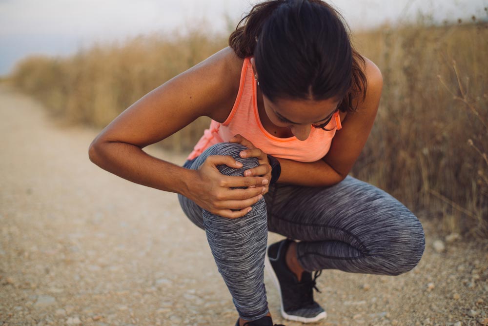 image of a female athlete suffering form running knee and arthritis during outdoor workout on dirt road.