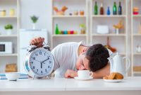 image of a man with alarm clock falling asleep at breakfast