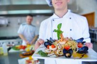 image of a chef dressed in white uniform decorating pasta salad and seafood fish in modern kitchen