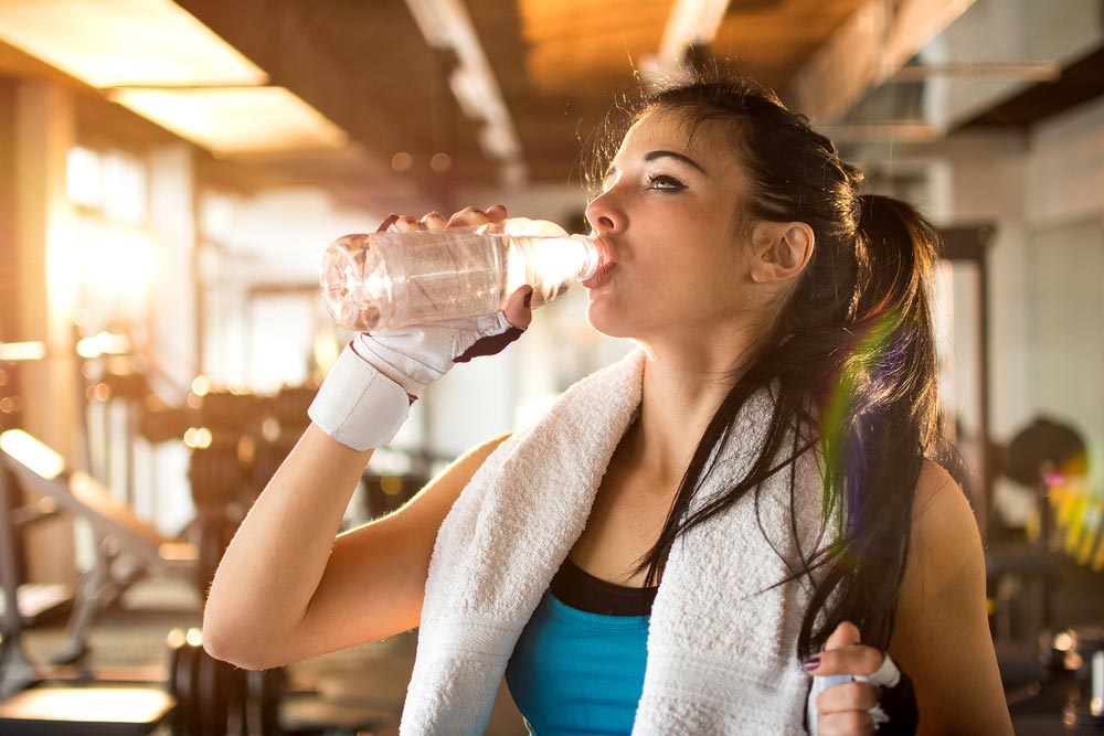 image of a young athletic woman drinking water in gym which will help her develop muscle hpertrophy