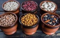 image of an assortment of beans on black wooden background. Soybean, red kidney bean, black bean,white bean, red bean and brown pinto beans