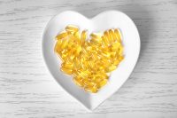image of Heart-shape plate with fish oil capsules on wooden background