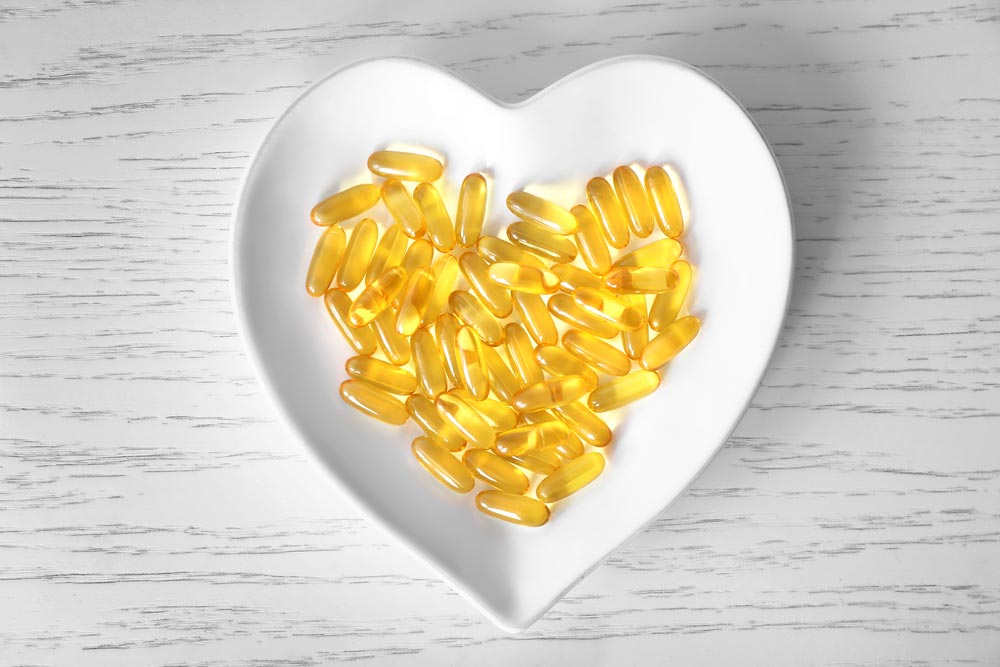 image of Heart-shape plate with fish oil capsules on wooden background