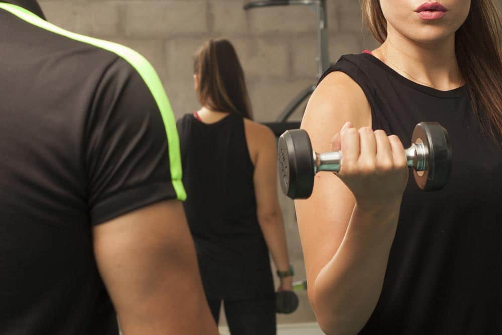 A female exerciser doing a one arm dumbbell curl. Are there people who are non-responders to strength training? Find out what science says about this issue.