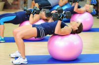 Cathe Friedrich on a pink stability ball strength training doing a close grip dumbbell bench press